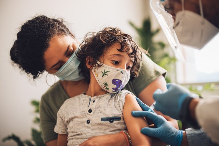 Parent comforting a masked child while a health worker gives a vaccine