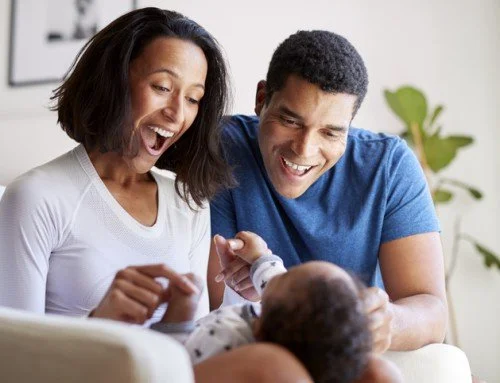 Two parents laughing together while playing with their baby