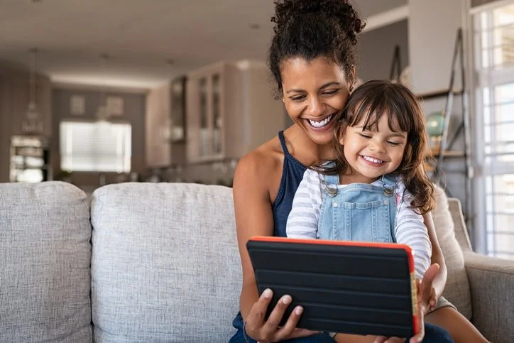 Parent and child smiling together while looking at a tablet