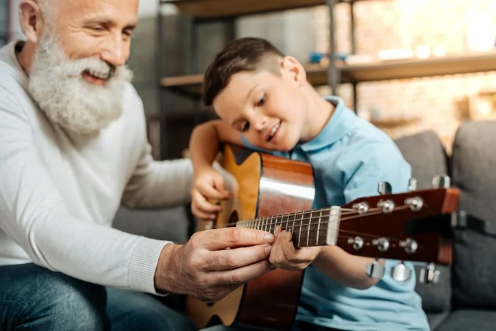 Grandparent teaching a child to play guitar together at home