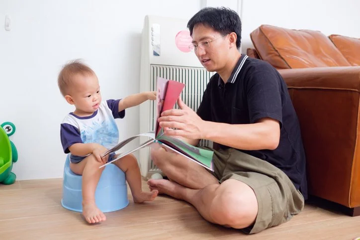 Toddler sitting on a potty-training seat while a parent sits nearby