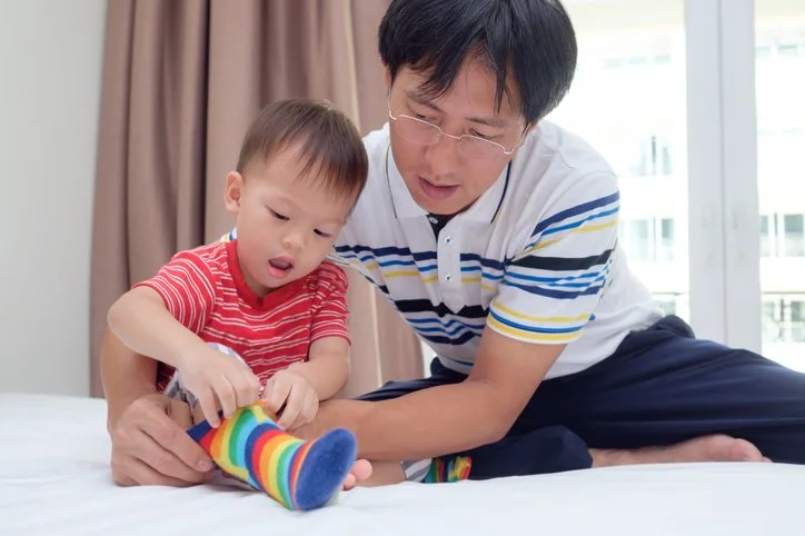 Parent and toddler playing with a toy together on the bed