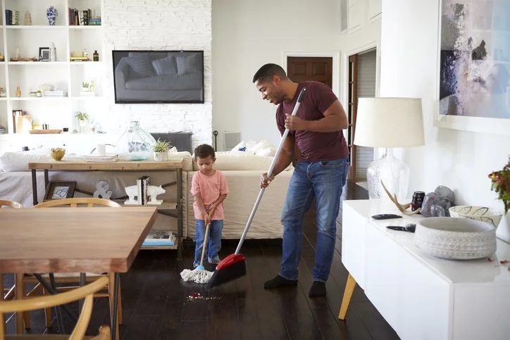 Parent and child sweeping the floor together at home