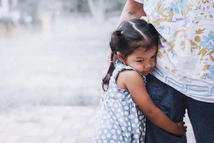 Child hugging a parent's leg tightly while standing outdoors
