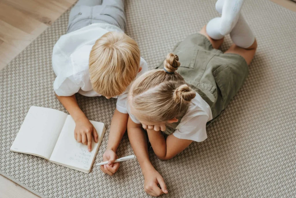 Two children lying on the floor writing together in a notebook