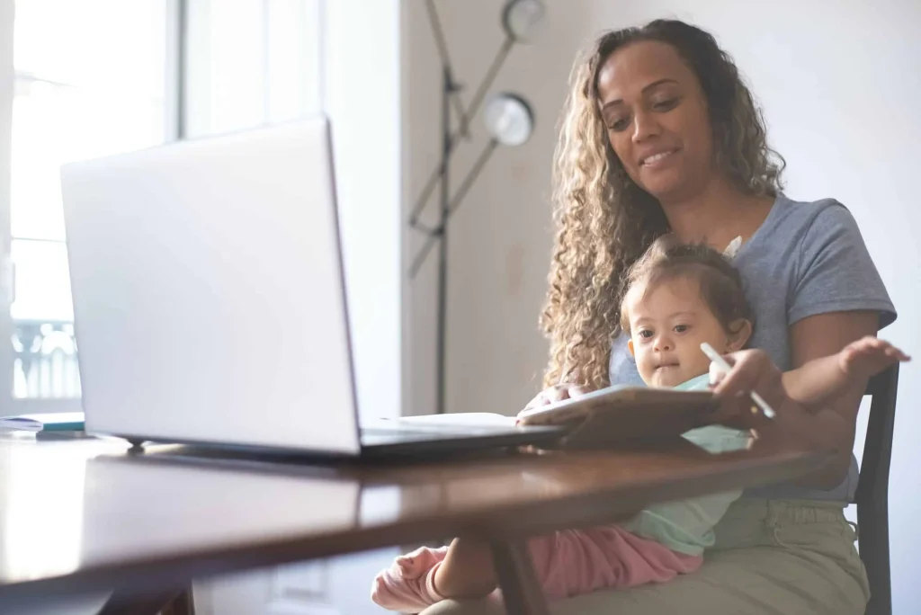 Parent working on a laptop while holding a baby