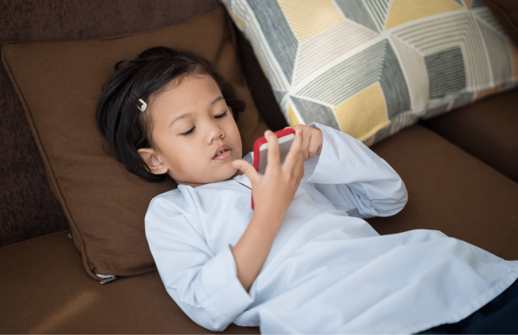 Child lying on the couch looking at a smartphone