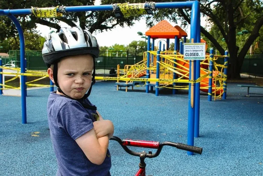 Child frowning with arms crossed next to a bike at a playground