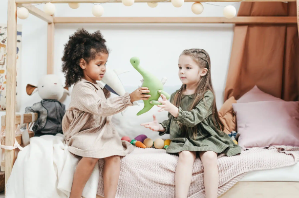 Two children sharing a toy dinosaur while sitting on a bed
