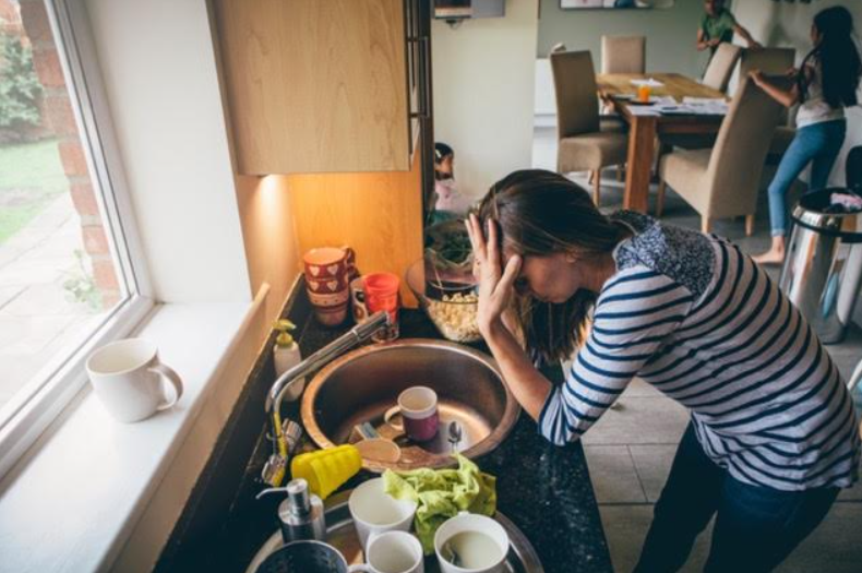 Parent standing at a sink full of dishes looking stressed