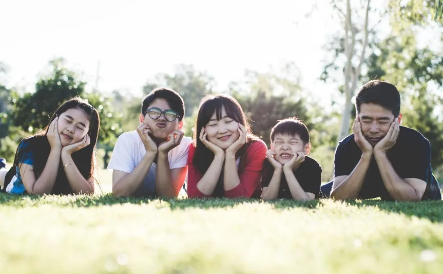Family of five lying together in the grass, smiling