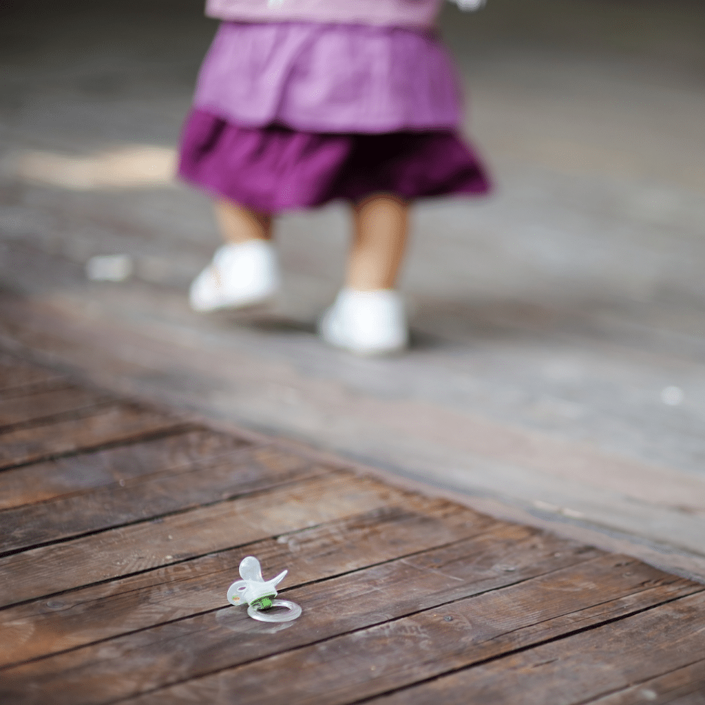 Toddler walking away alone on a deck, with a dropped pacifier nearby