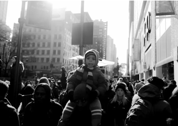 Child sitting on an adult's shoulders amid a large city crowd