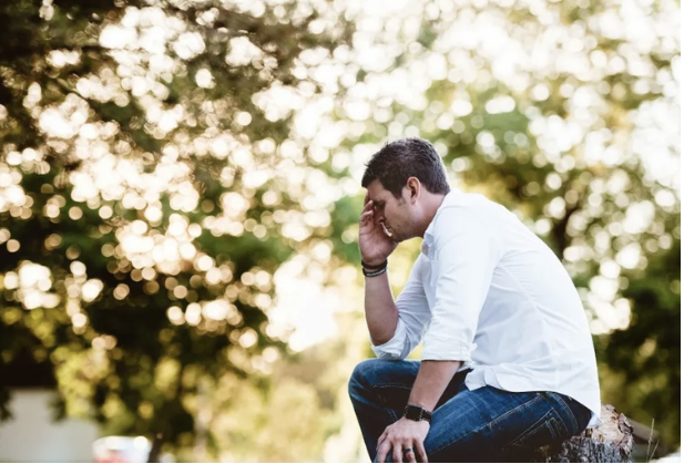 Man sitting outdoors with his head in his hand, looking stressed