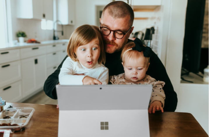 Father and two young children looking at a laptop screen together