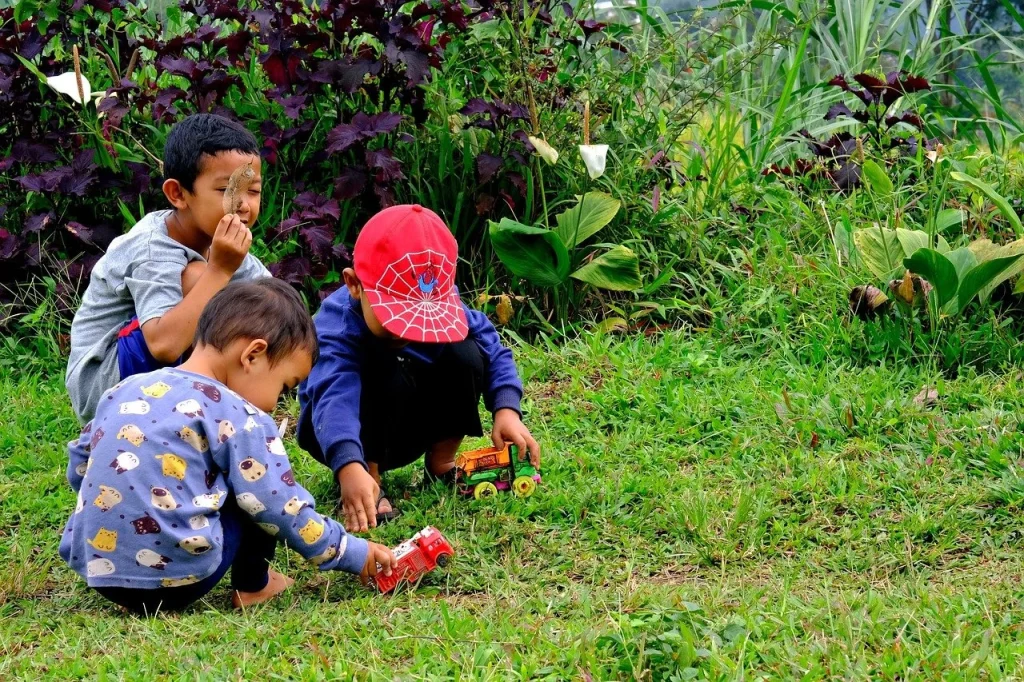 Three young children crouching outdoors, looking at something in a garden