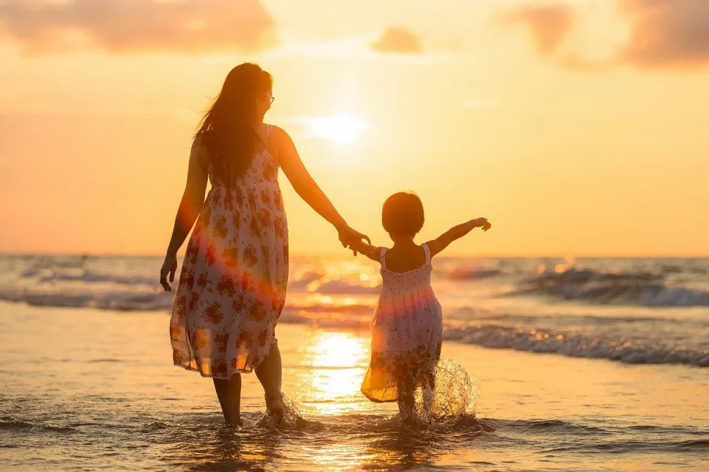 Parent and child walking hand in hand along the beach at sunset