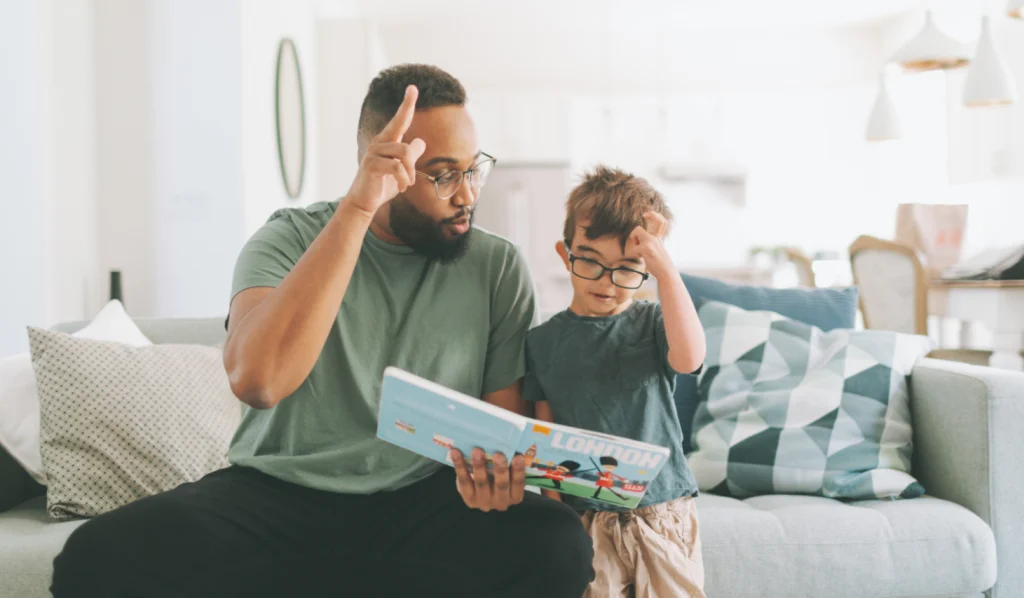 Father reading a picture book with his young son on the couch