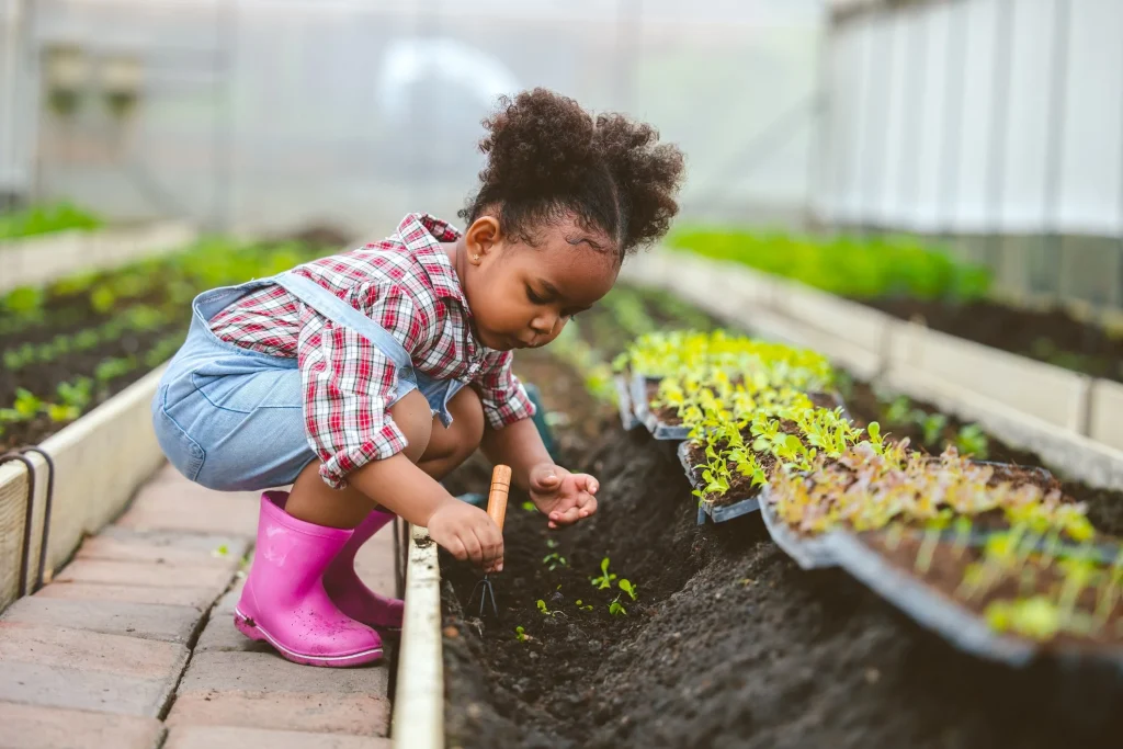 Young girl in rain boots planting seedlings in a greenhouse