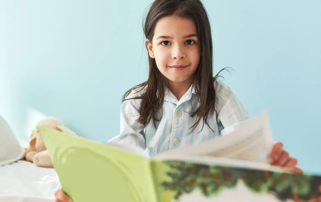 Girl sitting on her bed reading an open picture book