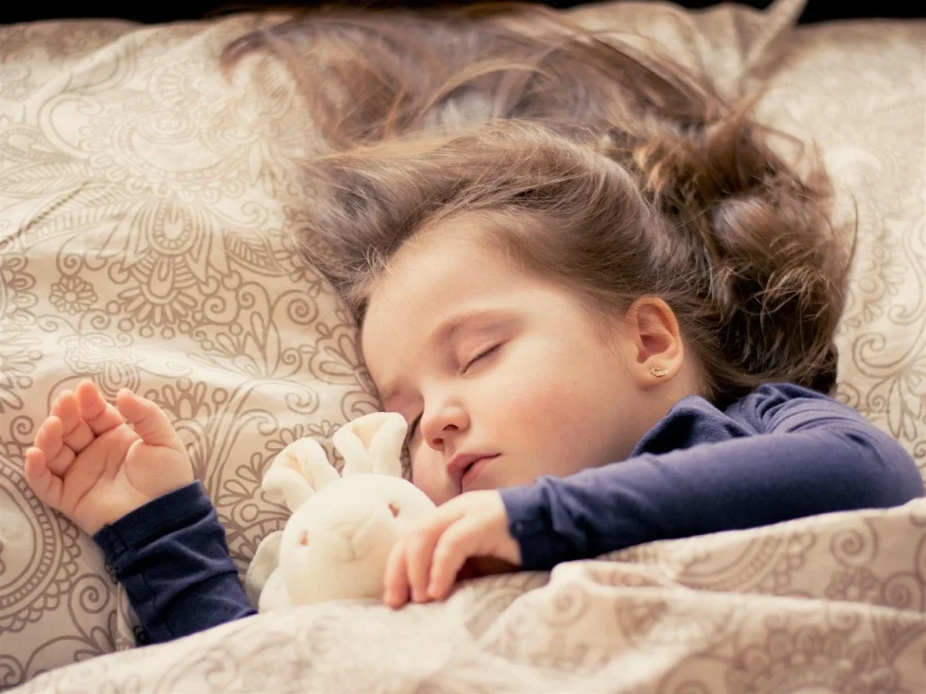 Young girl sleeping peacefully in bed with a stuffed bunny