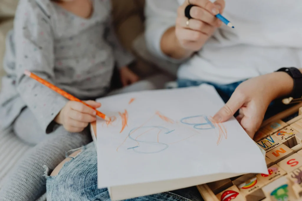 Child drawing on paper while an adult gently guides their hand