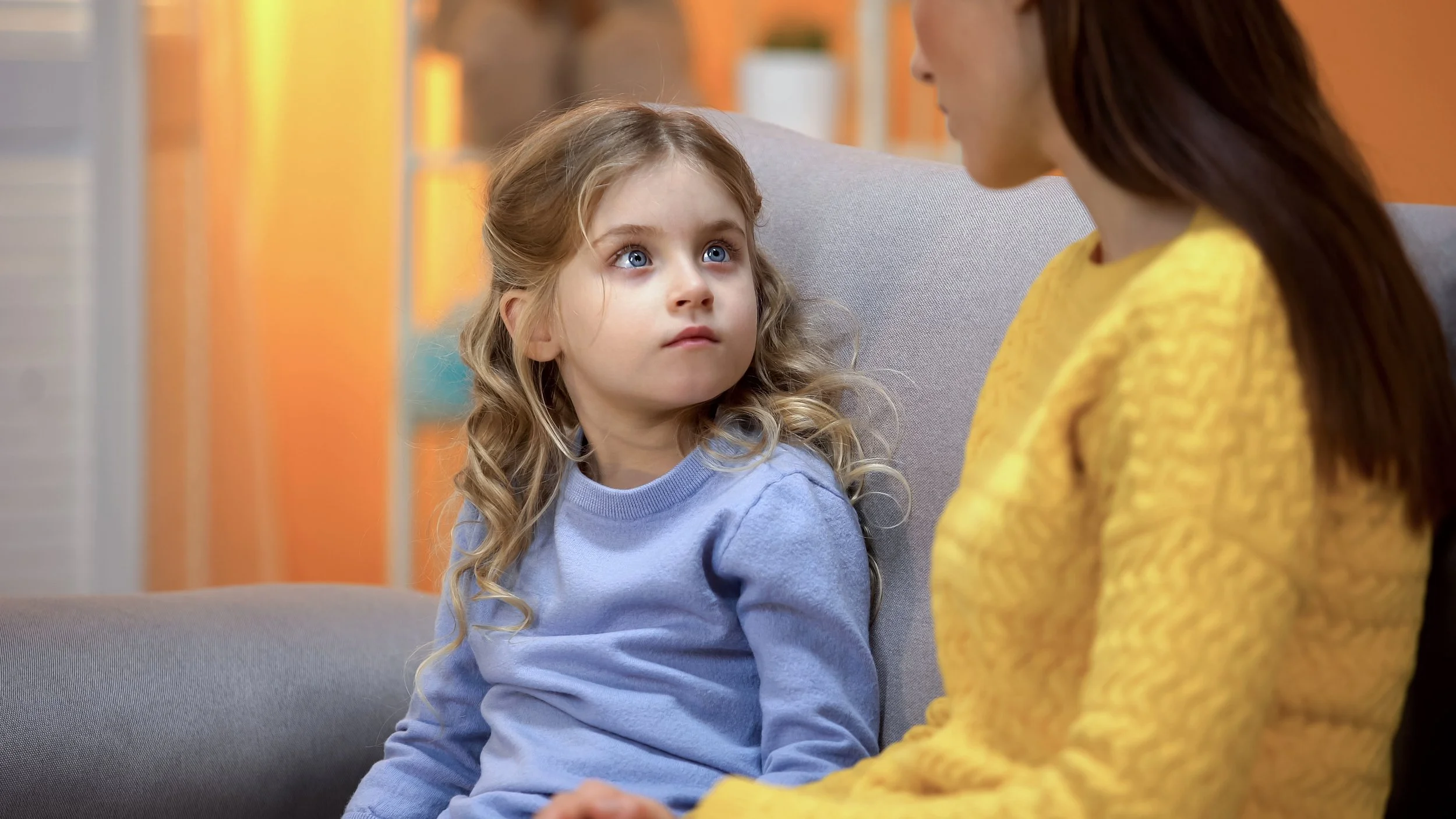 Worried-looking girl listening to an adult talk on the couch