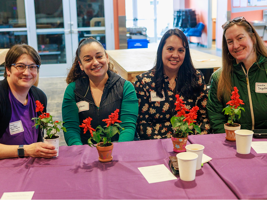 Four people smiling together at a table with small potted plants during an event
